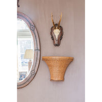 Decorative wall mirror with wicker shelf and deer head mount on a beige wall.