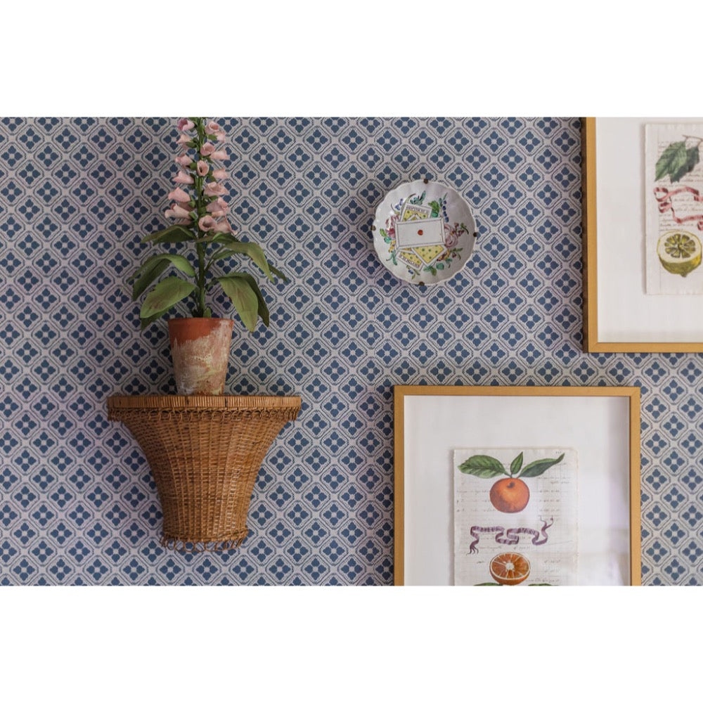 Decorative wall with patterned wallpaper, wicker shelf with plant, and framed prints.