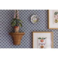 Decorative wall with patterned wallpaper, wicker shelf with plant, and framed prints.