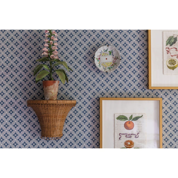 Decorative wall with patterned wallpaper, wicker shelf with plant, and framed prints.