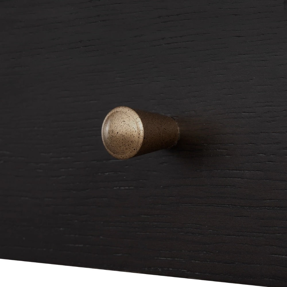 A close-up of a cylindrical cabinet knob with a speckled metallic bronze finish, mounted on a dark black wood drawer front.