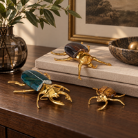 Three Currey & Company Brass + Marble Beetle Colony sculptures sit on a table beside a book and glass vase.