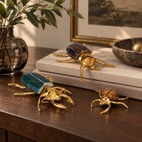 Three Currey & Company Brass + Marble Beetle Colony sculptures sit on a table beside a book and glass vase.