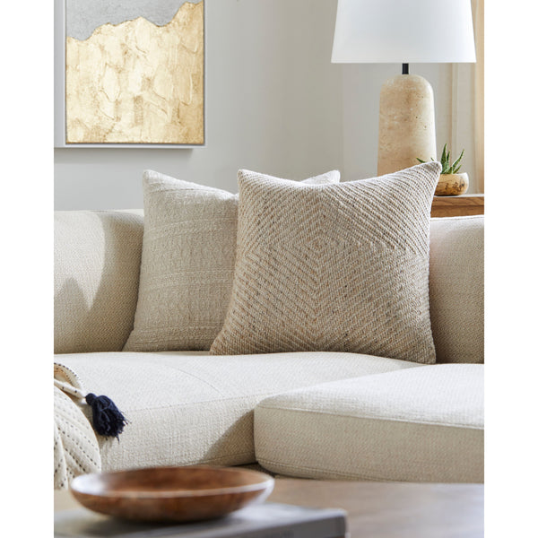 Inviting living room featuring a beige sectional sofa, Surya's Indoor/Outdoor Cairn Woven Pillow crafted from fade-resistant material for added texture, complemented by a wooden bowl and a lamp on the side table.