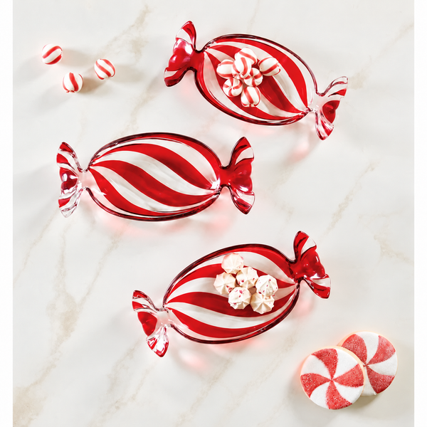 Three red and white striped candy-shaped glass dishes arranged on a light marble surface, styled with peppermint candies and small white flowers.