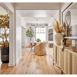 Bright dining room featuring a wooden floor and a modern table, complemented by the Phillips Scott Havana Seagrass Woven Chairs that add a coastal vibe. The space is accented with plants and large vases, while a large window allows natural light to flood in.