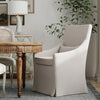 Elegant dining area with a Beige Linen Skirted Armchair by Sarreid, Ltd., round wooden table, and a leafy plant.