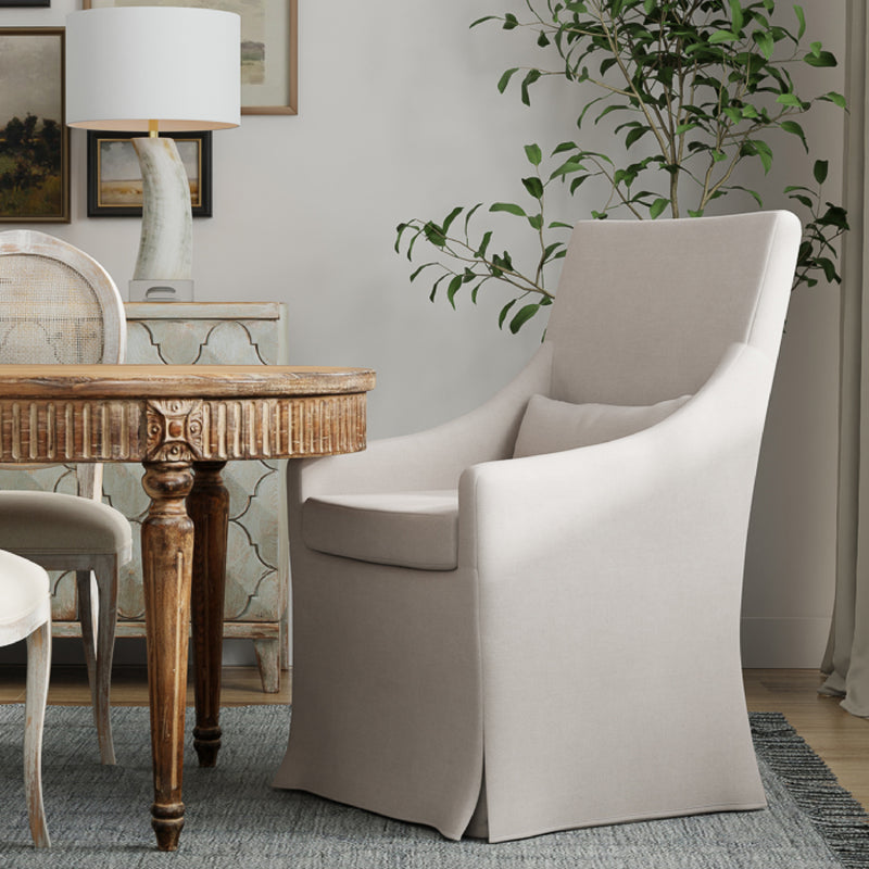 Elegant dining area with a Beige Linen Skirted Armchair by Sarreid, Ltd., round wooden table, and a leafy plant.