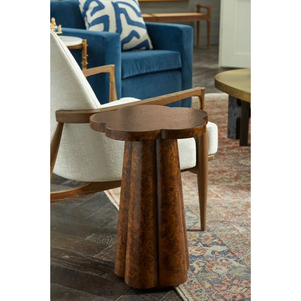 A rustic, scalloped-edge wooden end table with a flared pedestal base, shown in a styled living room setting next to a cream upholstered chair.