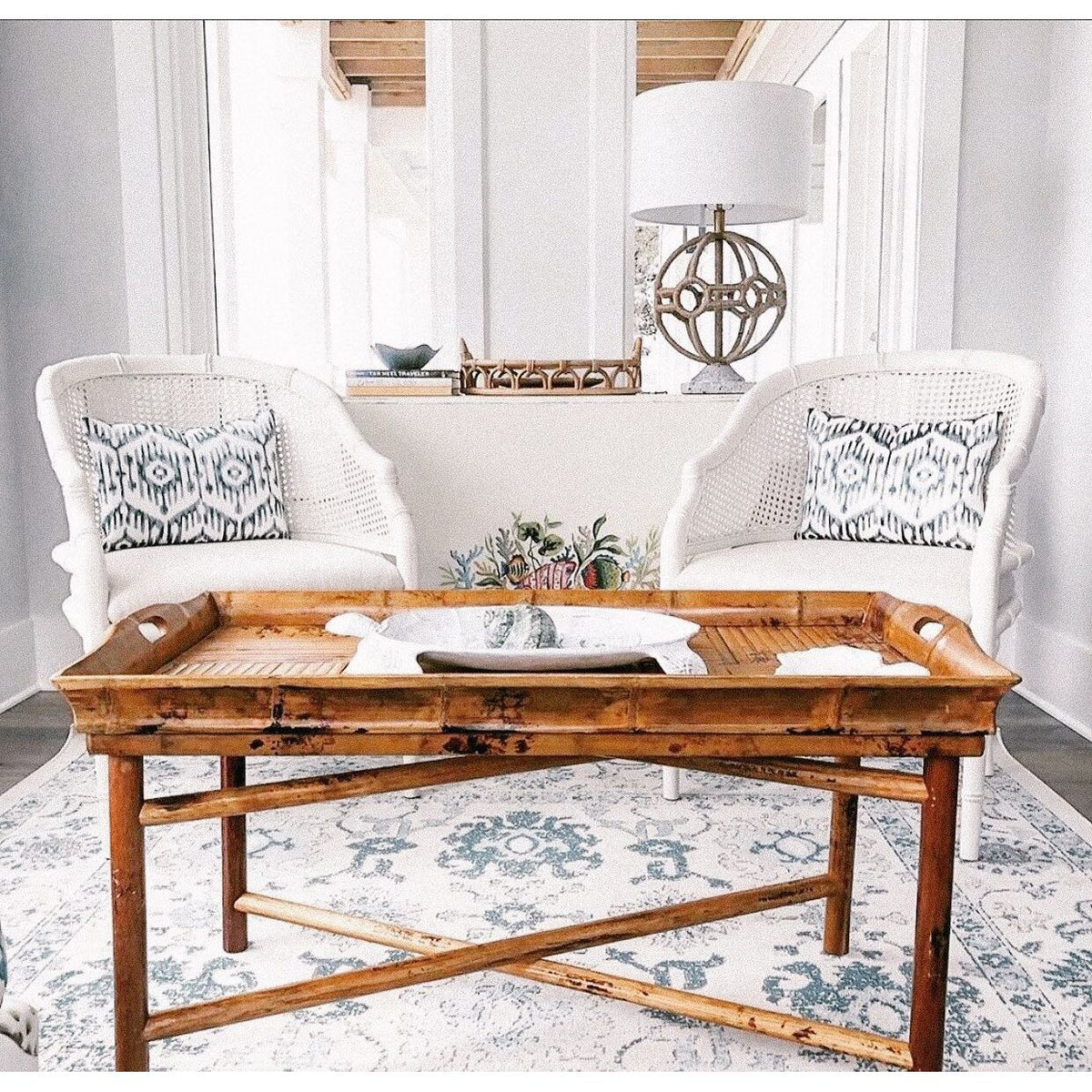 Two white wicker chairs with patterned pillows and a Kenian Tortoise Shell Bamboo Butler Table in a bright living room.
