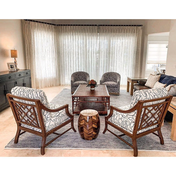 A modern living room with patterned chairs, sheer curtains, and a Kenian Pagoda Rattan + Bamboo Coffee Table.