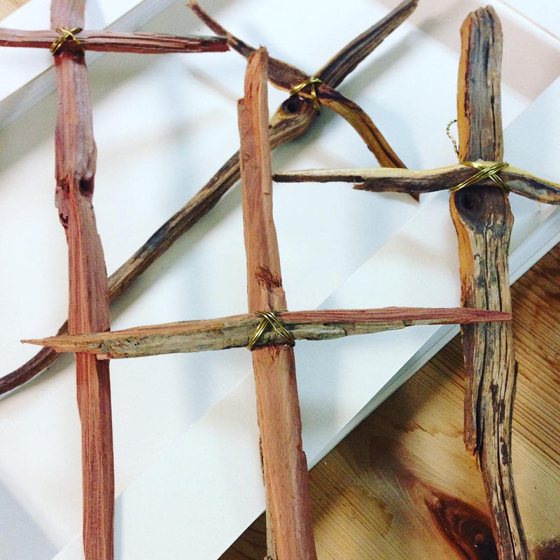 Three rustic crosses made of rough wooden sticks, tied together with thin wire, are displayed on a white surface. The wood, in various shades of brown with visible texture and grain, is beautifully complemented by the Gold + Silver Rustic Cross in Frame - Small from Shadow Catchers Art at the center.