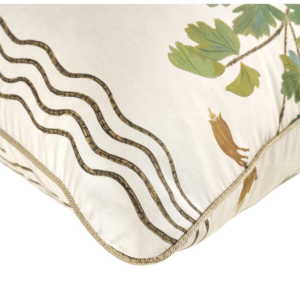 Close-up of a decorative throw pillow corner showing a cream fabric base with embroidered wavy dark brown lines, green leaves, and small brown bird motifs, finished with a gold-toned piped edge.