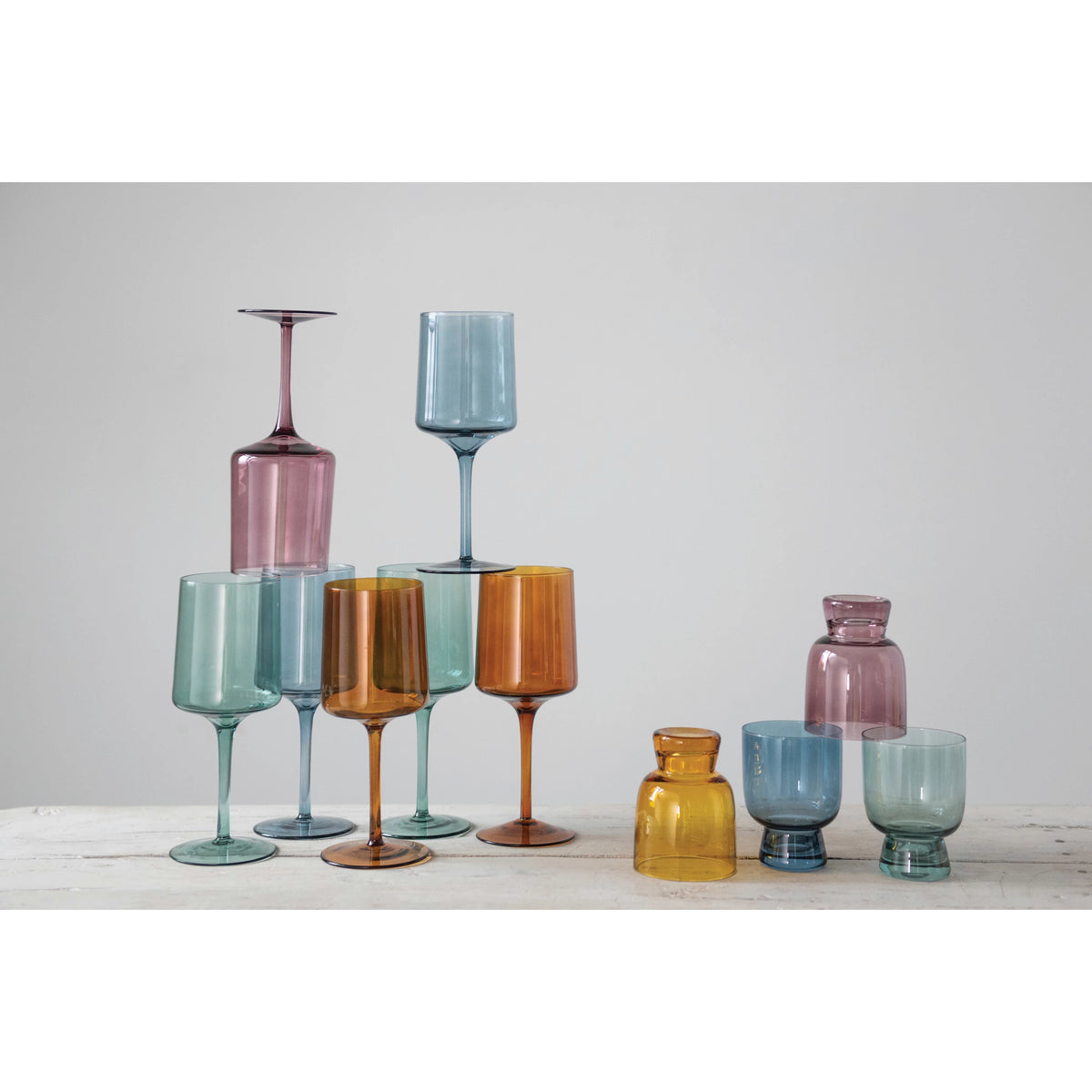 The table features an eye-catching glassware arrangement with Creative Co-Op's Colored Stemmed Wine Glasses (set of 4), accompanied by pieces in blue, pink, yellow, and purple, each boasting unique shapes and sizes.