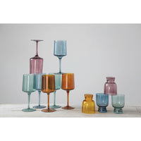The table features an eye-catching glassware arrangement with Creative Co-Op's Colored Stemmed Wine Glasses (set of 4), accompanied by pieces in blue, pink, yellow, and purple, each boasting unique shapes and sizes.