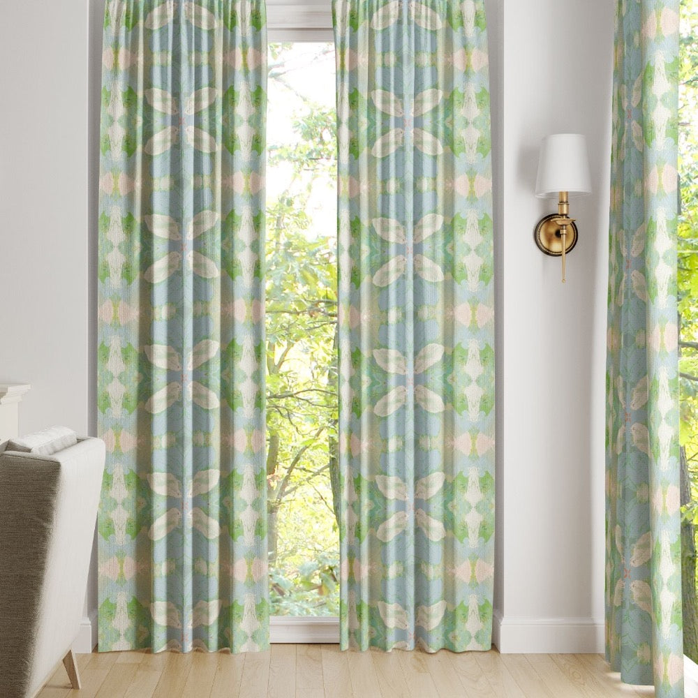Light blue and green Elephant Falls Curtain Panels by Laura Park Designs hang before a window with trees outside.