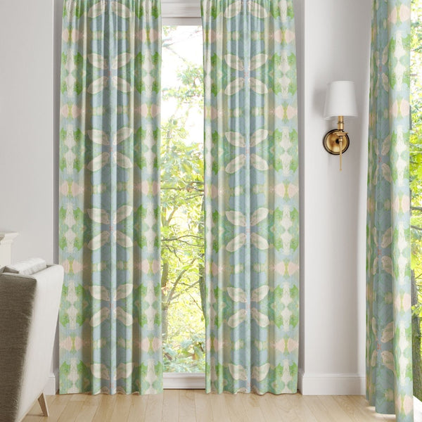 Light blue and green Elephant Falls Curtain Panels by Laura Park Designs hang before a window with trees outside.
