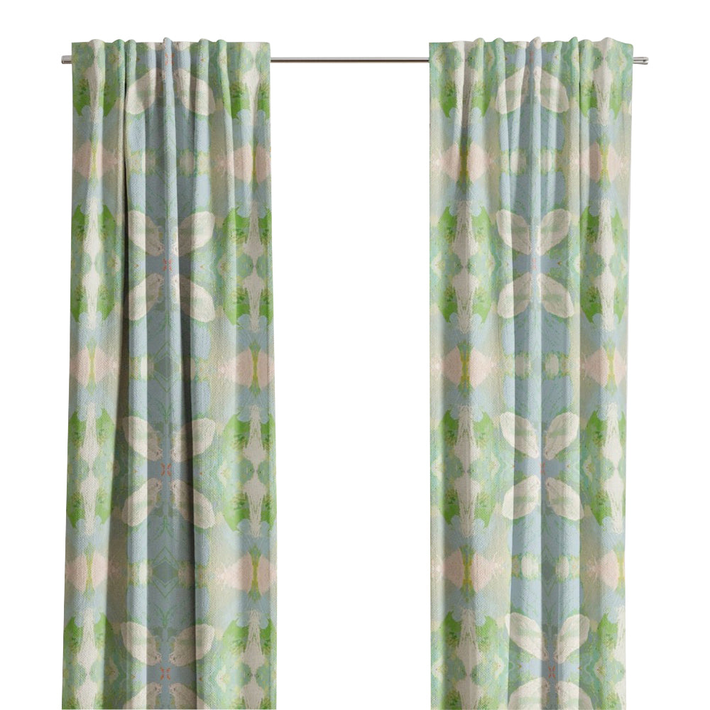 Light blue and green Elephant Falls Curtain Panels by Laura Park Designs hang before a window with trees outside.