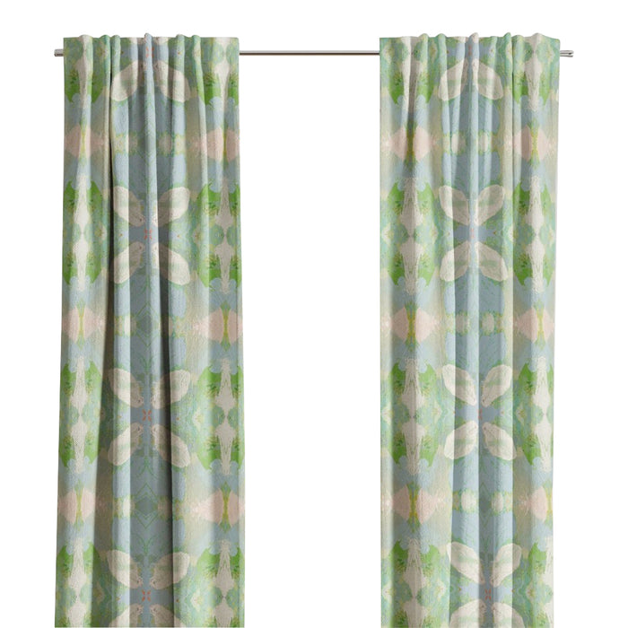 Light blue and green Elephant Falls Curtain Panels by Laura Park Designs hang before a window with trees outside.