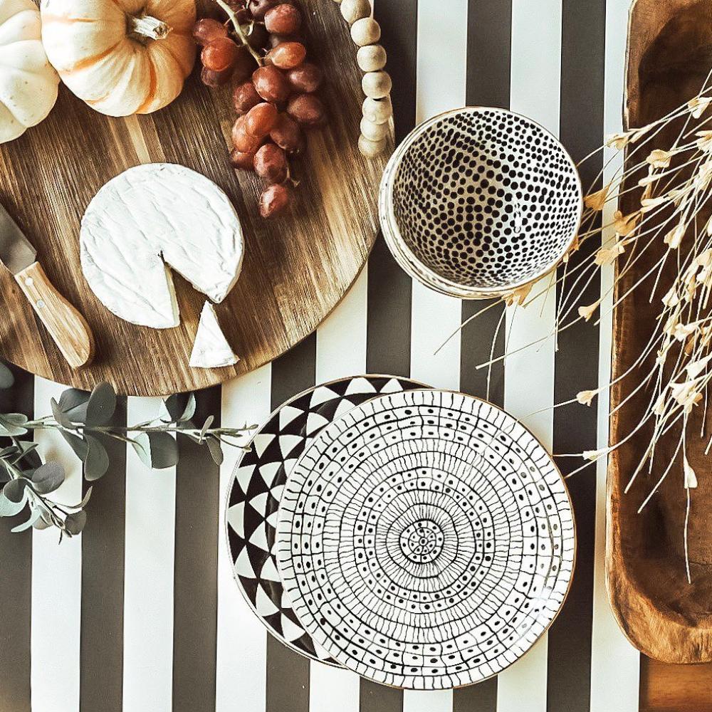 Wooden cutting board with cheese, grapes, and a decorative bowl on a black and white striped background.
