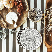 Wooden cutting board with cheese, grapes, and a decorative bowl on a black and white striped background.
