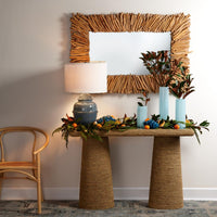 Decorative table with a lamp, plants, and a mirror with a natural frame in a room.