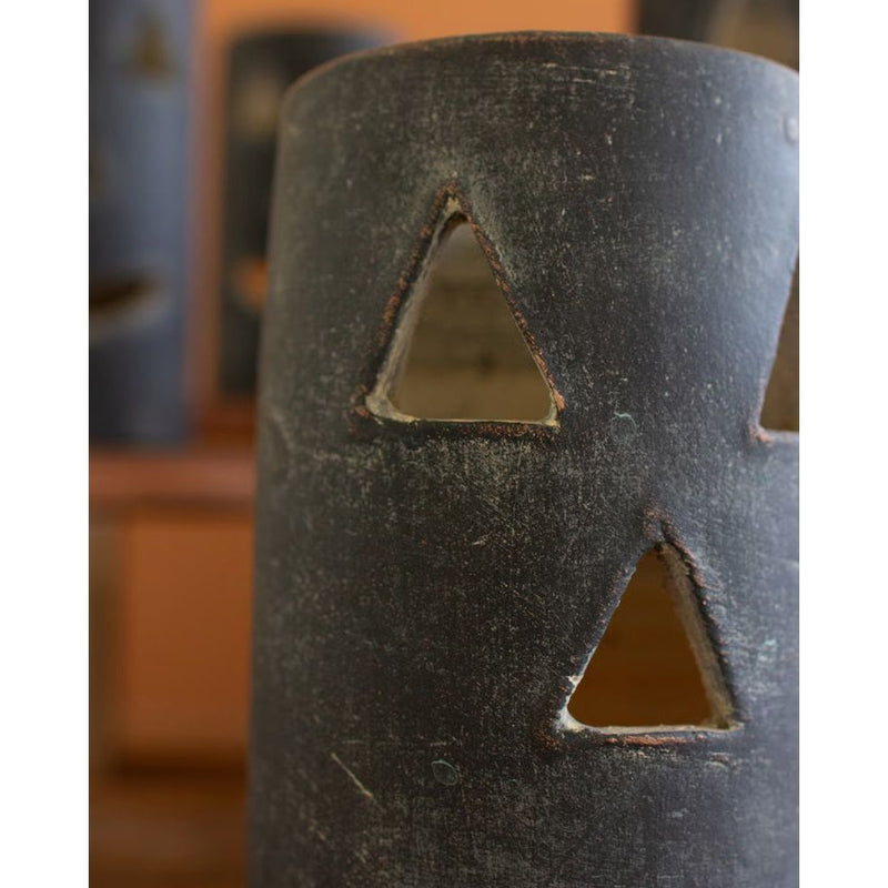 Close-up of a weathered metal cylinder with triangular cutouts, exuding a Halloween charm, set against a blurred background. Featured is one of Kalalou's Black Clay Jack-O-Lanterns from their set of six.