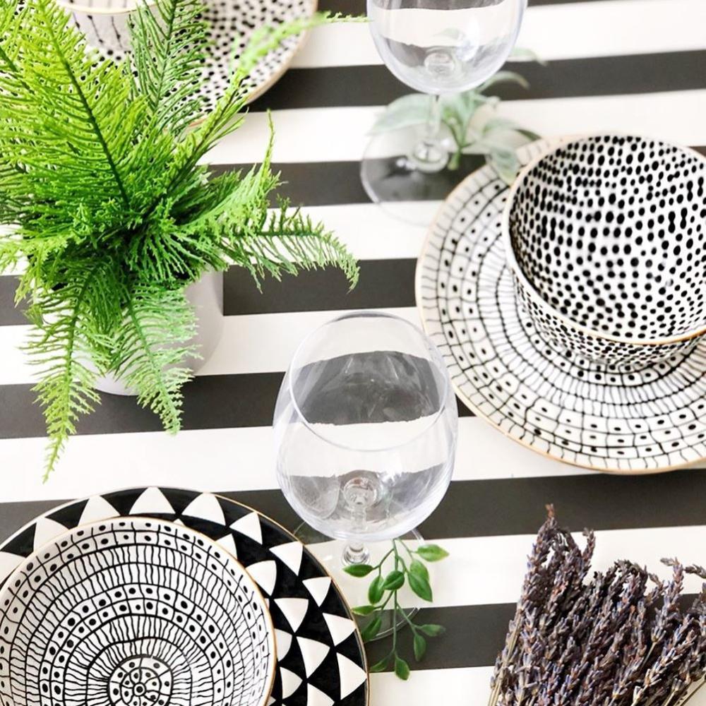 Black and white patterned tableware on a black and white striped tablecloth with greenery.