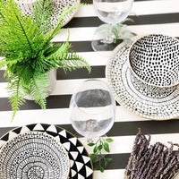 Black and white patterned tableware on a black and white striped tablecloth with greenery.