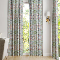 Martini Olives Curtain Panels by Laura Park Designs hang by a window, letting in natural light near an armchair.
