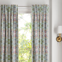 Martini Olives Curtain Panels by Laura Park Designs hang over a window with greenery outside and a wall sconce on the right.