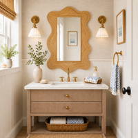 Beige bathroom with Drift Natural Rattan Mirror by Woodbridge Furniture, gold fixtures, twin lights, plants, towels.