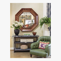 Decorative interior with a large octagonal mirror, green armchair, and table with decor items.
