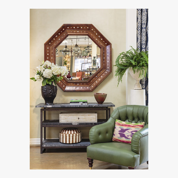 Decorative interior with a large octagonal mirror, green armchair, and table with decor items.