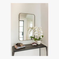 A potted white orchid, books, and crystals on a black table beneath Mirror Home’s Leather Wrapped Antique Bronze Mirror.