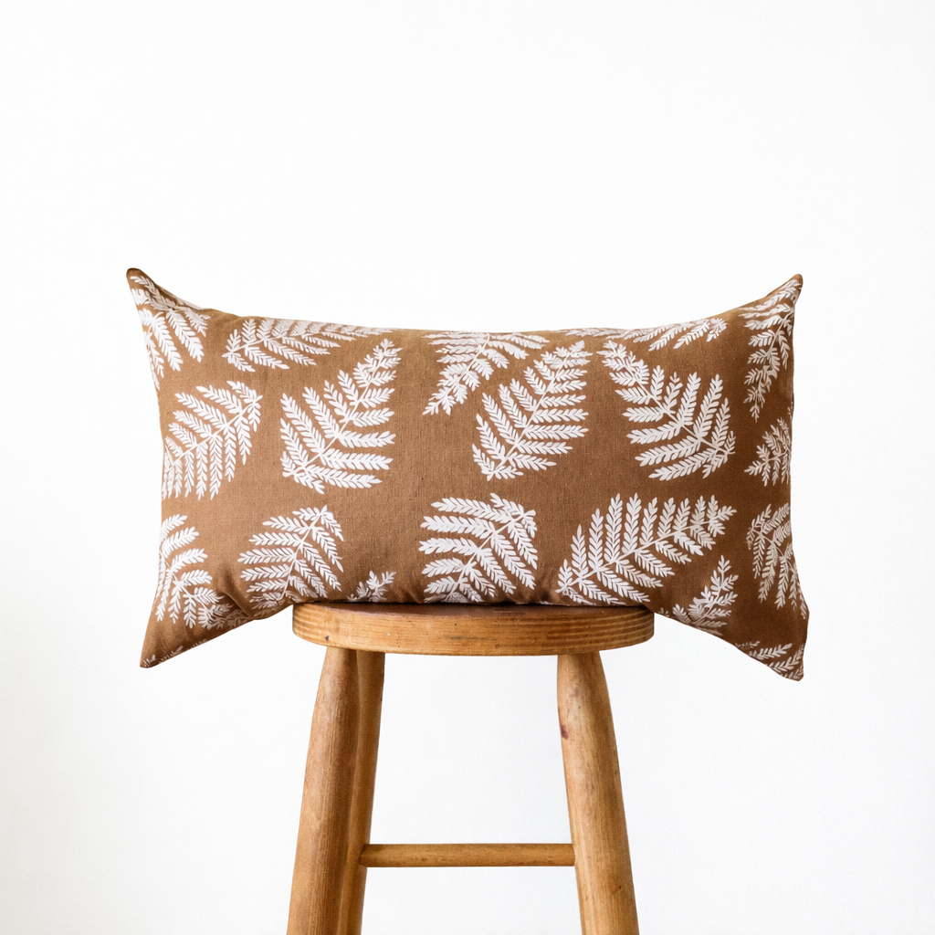 Ginger Brown + White Ferns Lumbar Pillow by Muse Textiles, displayed on a stool against a white background.