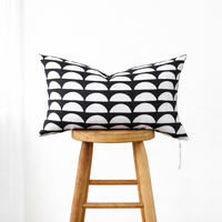 Muse Textiles Dark Gray + White Half Moons Lumbar Pillow, hand-crafted and shown on a wooden stool against white.