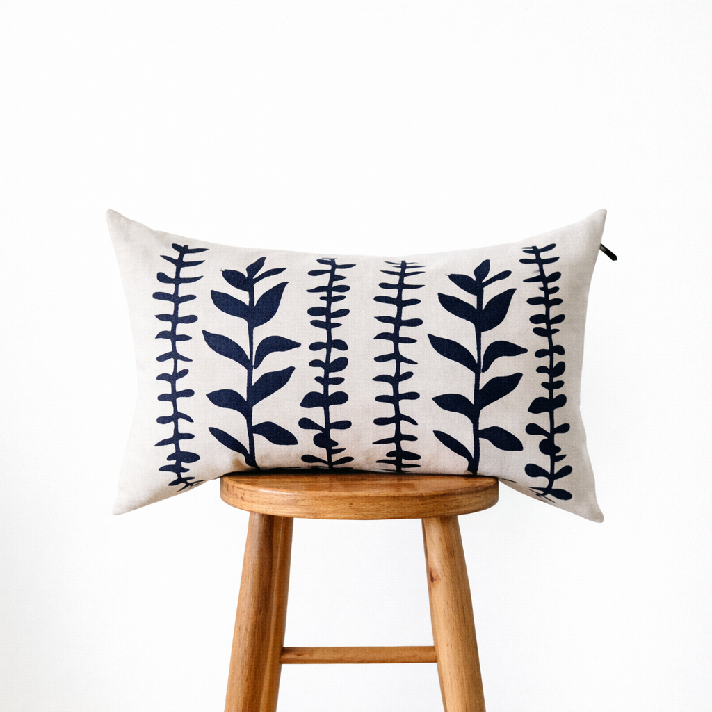 Hand-crafted in Atlanta, the Muse Textiles Navy Eucalyptus Lumbar Pillow rests on a wooden stool against a white background.