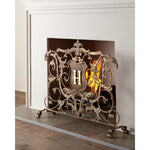Dr. Livingstone, I Presume's Light Burnished Gold Fireplace Screen with "H" shield and Fleur de Lis, in front of a lit fire.