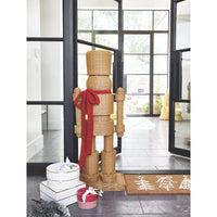 The Santa Barbara Design Studio All Weather Rattan Nutcracker with Red Bow stands by gifts and festive décor near glass doors.