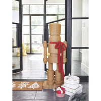 The All Weather Rattan Nutcracker with Red Bow by Santa Barbara Design Studio stands by gift boxes in a festive entryway.
