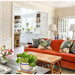 Bright living room with an orange sofa, floral pillows, plants, and a Kenian Antique Tortoise Shell Bamboo Ottoman.