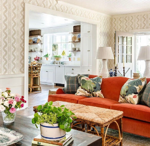 Bright living room with an orange sofa, floral pillows, plants, and a Kenian Antique Tortoise Shell Bamboo Ottoman.