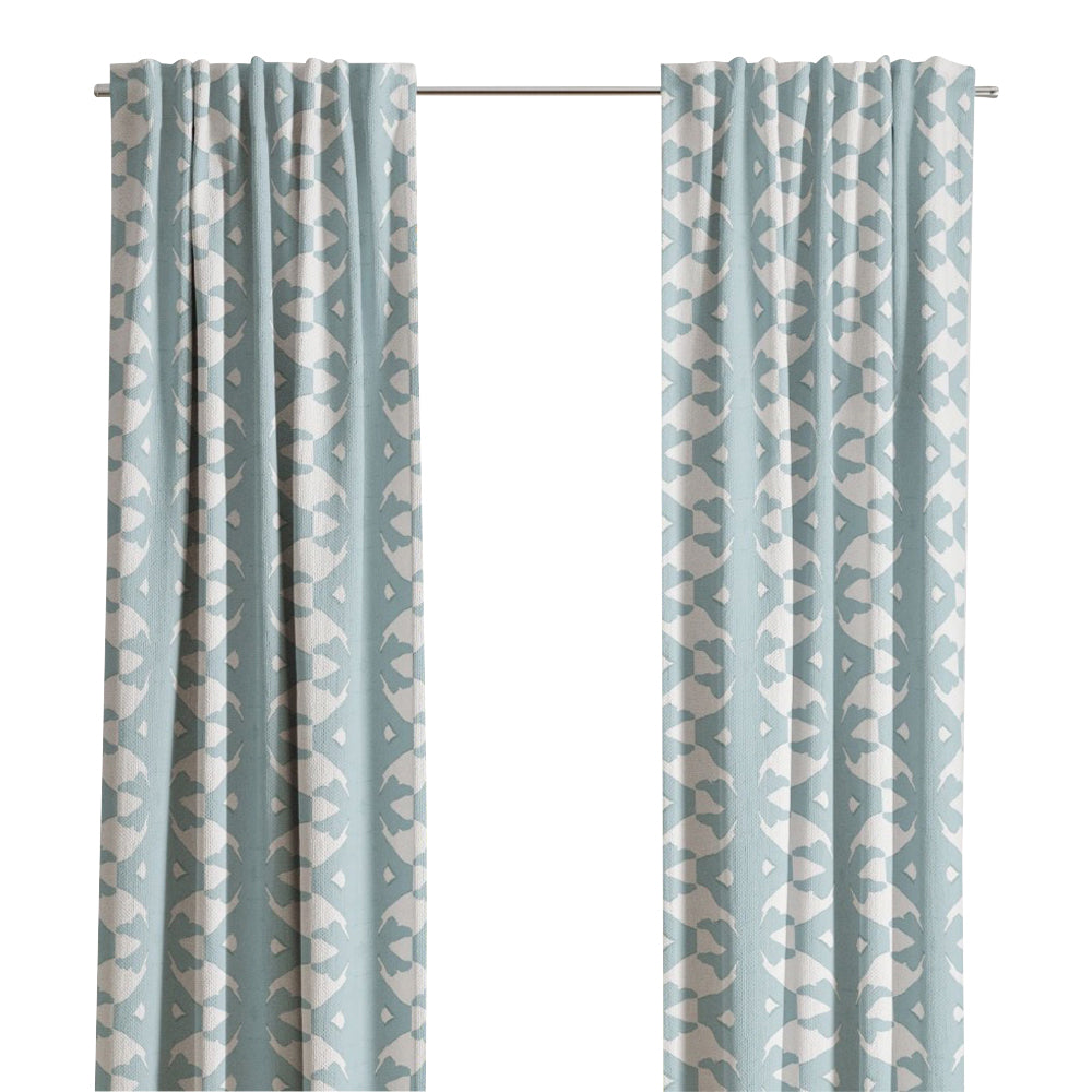 Laura Park Designs' Palm Mist Curtain Panels in light blue with a white geometric pattern hang by a window.