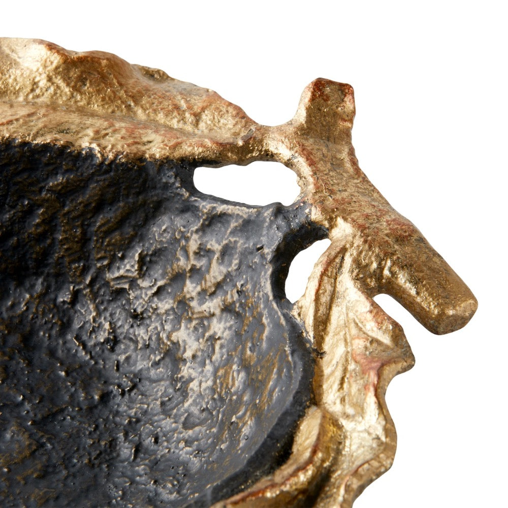 Close-up of a textured sculptural bow; with a dark charcoal-black interior and a metallic gold-toned outer edge, shown against a plain white background.