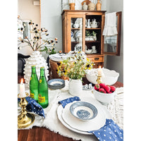 A dining table set featuring Always Relish's BPA-free Scalloped White Melamine Dinner Plates (set of 4), adorned with drinks, flowers, candles, and strawberries, with a cabinet of dishes in the background.