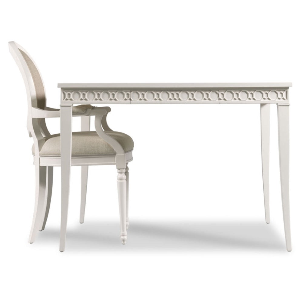 A white dining table with a decorative carved apron and matching white armchairs with beige upholstered seats, shown on a clean white background.
