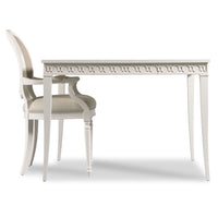 A white dining table with a decorative carved apron and matching white armchairs with beige upholstered seats, shown on a clean white background.