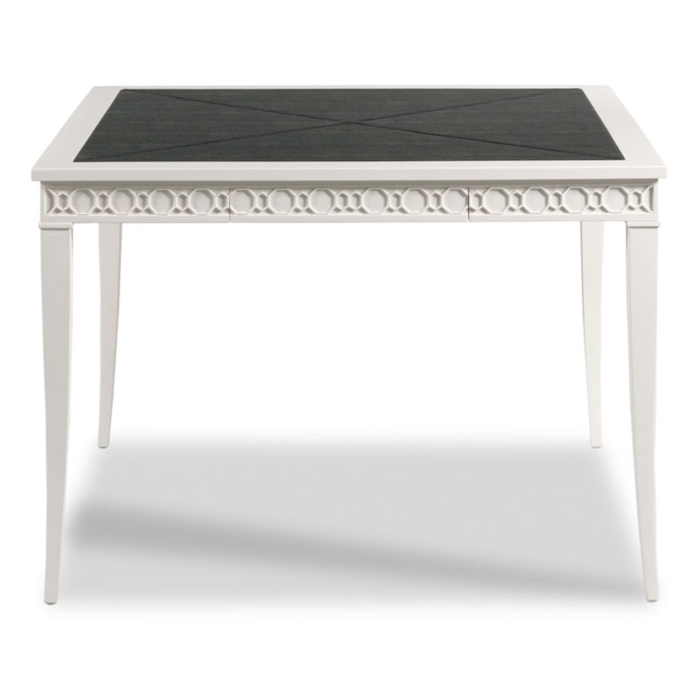 A white dining table with a black textured square tabletop, featuring decorative circular cutout detailing along the apron and tapered legs.