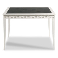 A white dining table with a black textured square tabletop, featuring decorative circular cutout detailing along the apron and tapered legs.